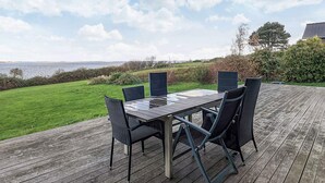 An outdoor deck with a table and chairs, overlooking a grassy area and the sea. - 8 Person Holiday Home in Olsted-by Traum (Olsted)