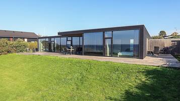 A modern house with a glass facade, a patio with outdoor furniture, and a well-maintained lawn.