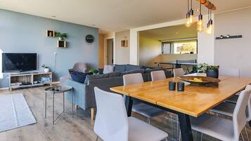 A modern living room with a dining area, a television, and a kitchen in the background.