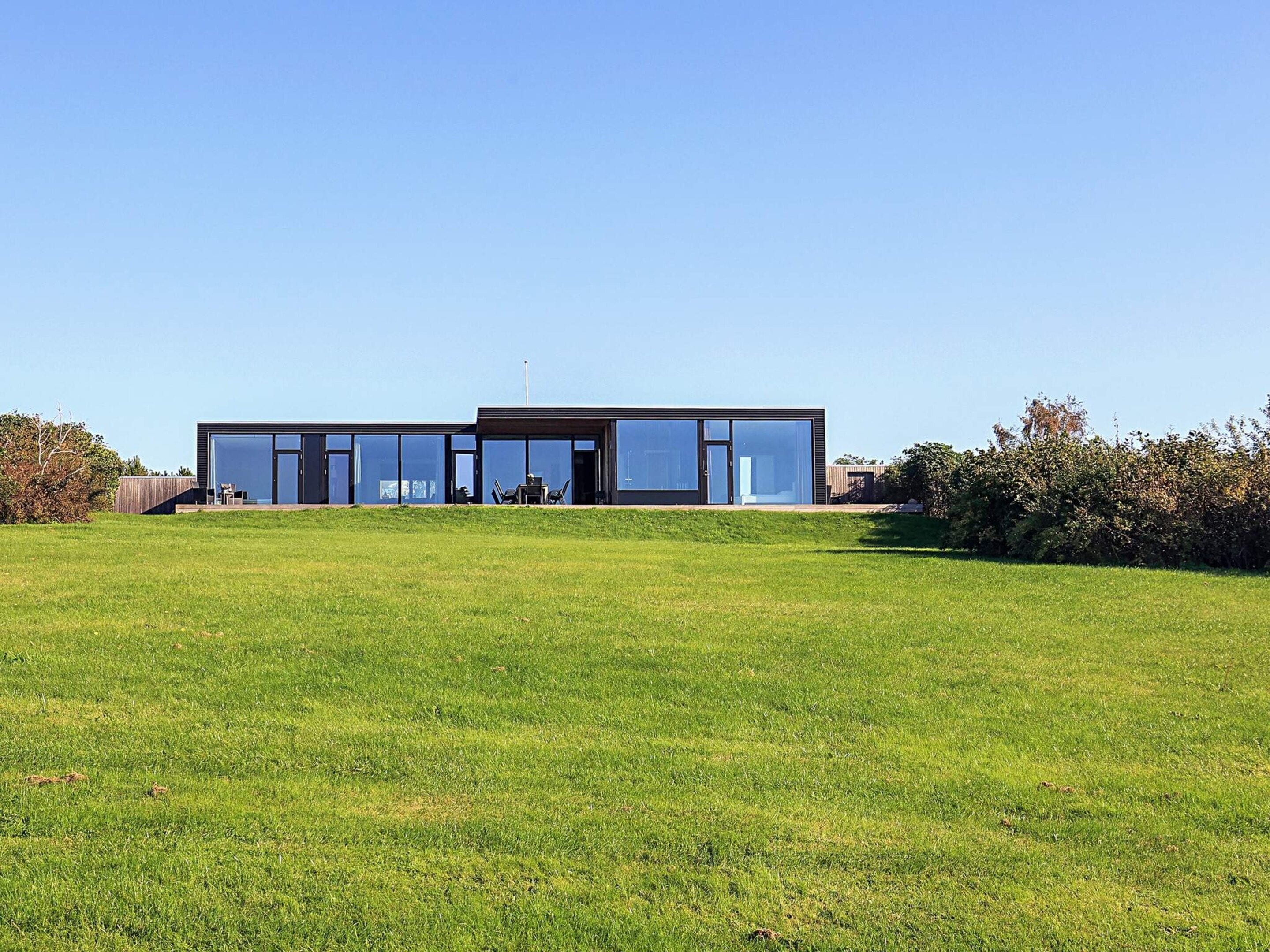 A modern two-story building with large glass windows, a flat roof, and a grassy lawn in front.