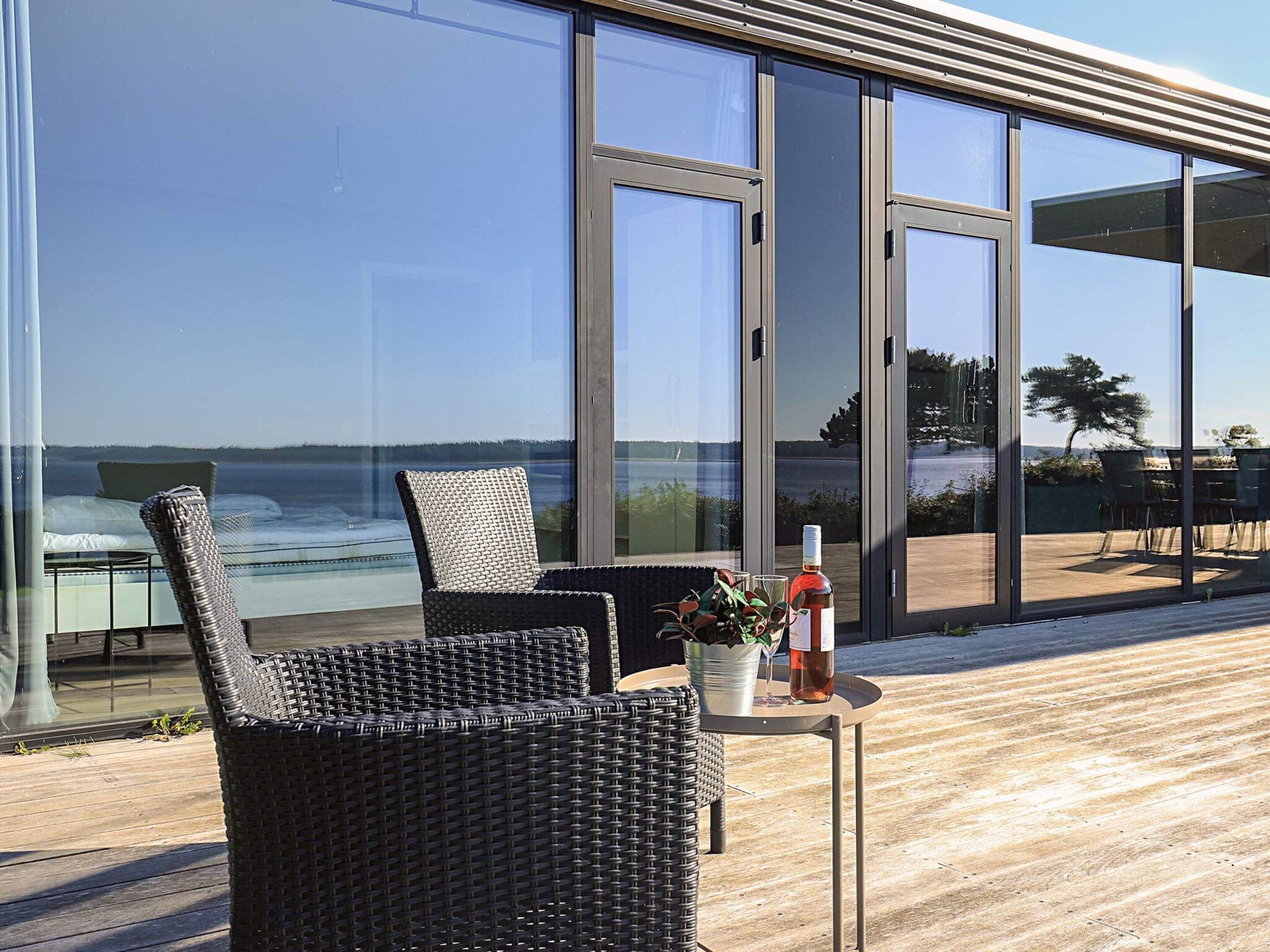 A modern outdoor seating area with wicker chairs and a table, overlooking a body of water.