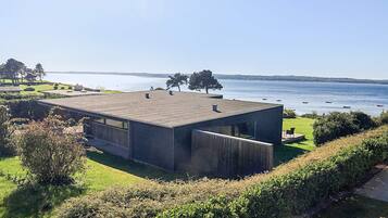 A modern house with a flat roof, large windows, and a view of the sea.