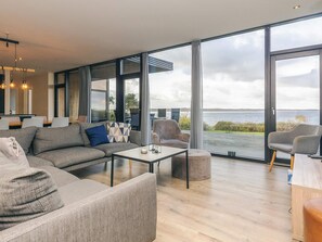 A modern living room with a large window offering a view of the sea. There is a sofa, a coffee table, and two chairs. - 8 Person Holiday Home in Olsted-by Traum (Olsted)