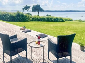 A deck with wicker chairs, a small round table, and a bottle of red wine. - 8 Person Holiday Home in Olsted-by Traum (Olsted)