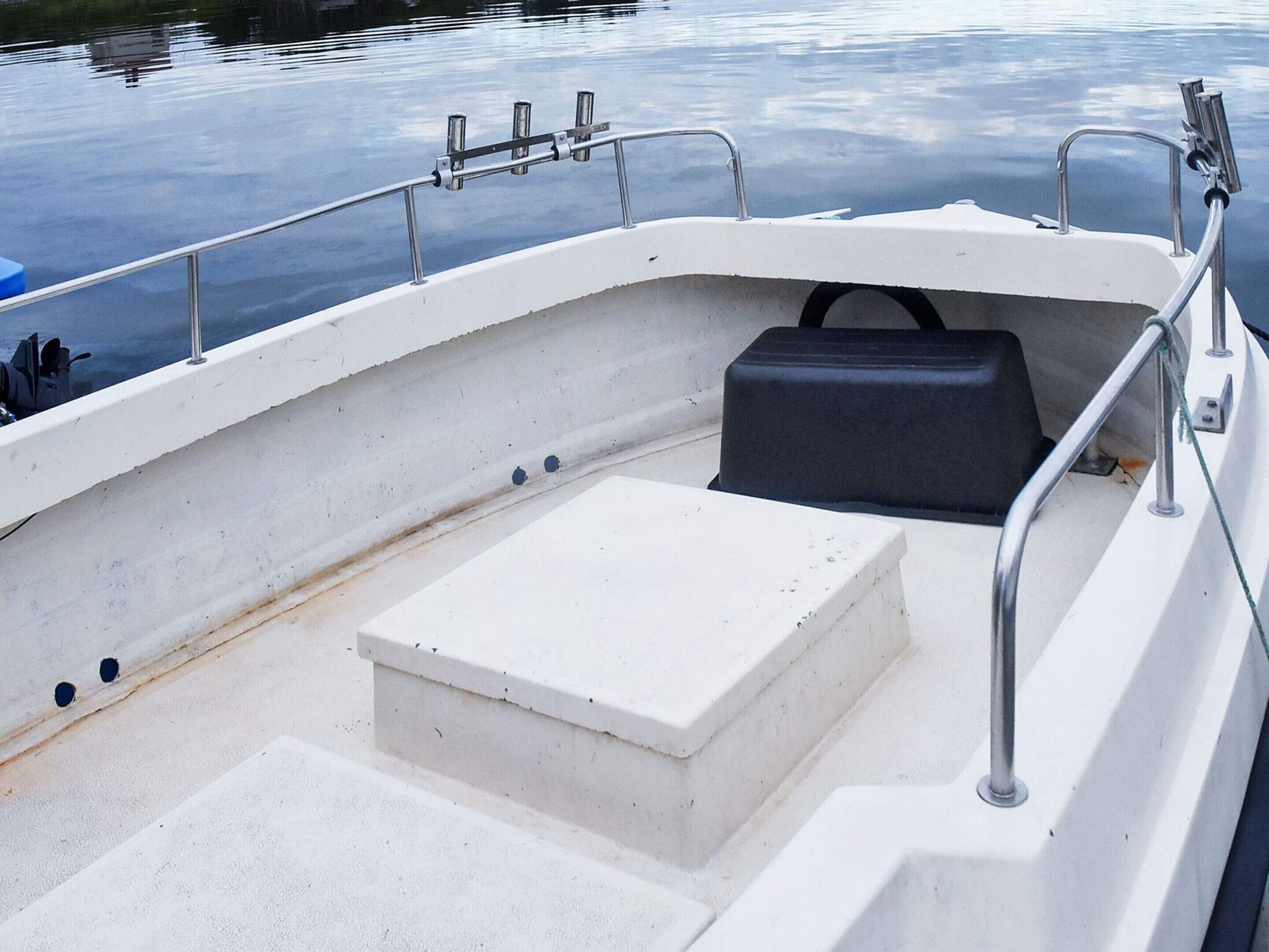 L'intérieur d'un bateau, avec un pont blanc, un coffre de rangement noir et des garde-corps en métal.