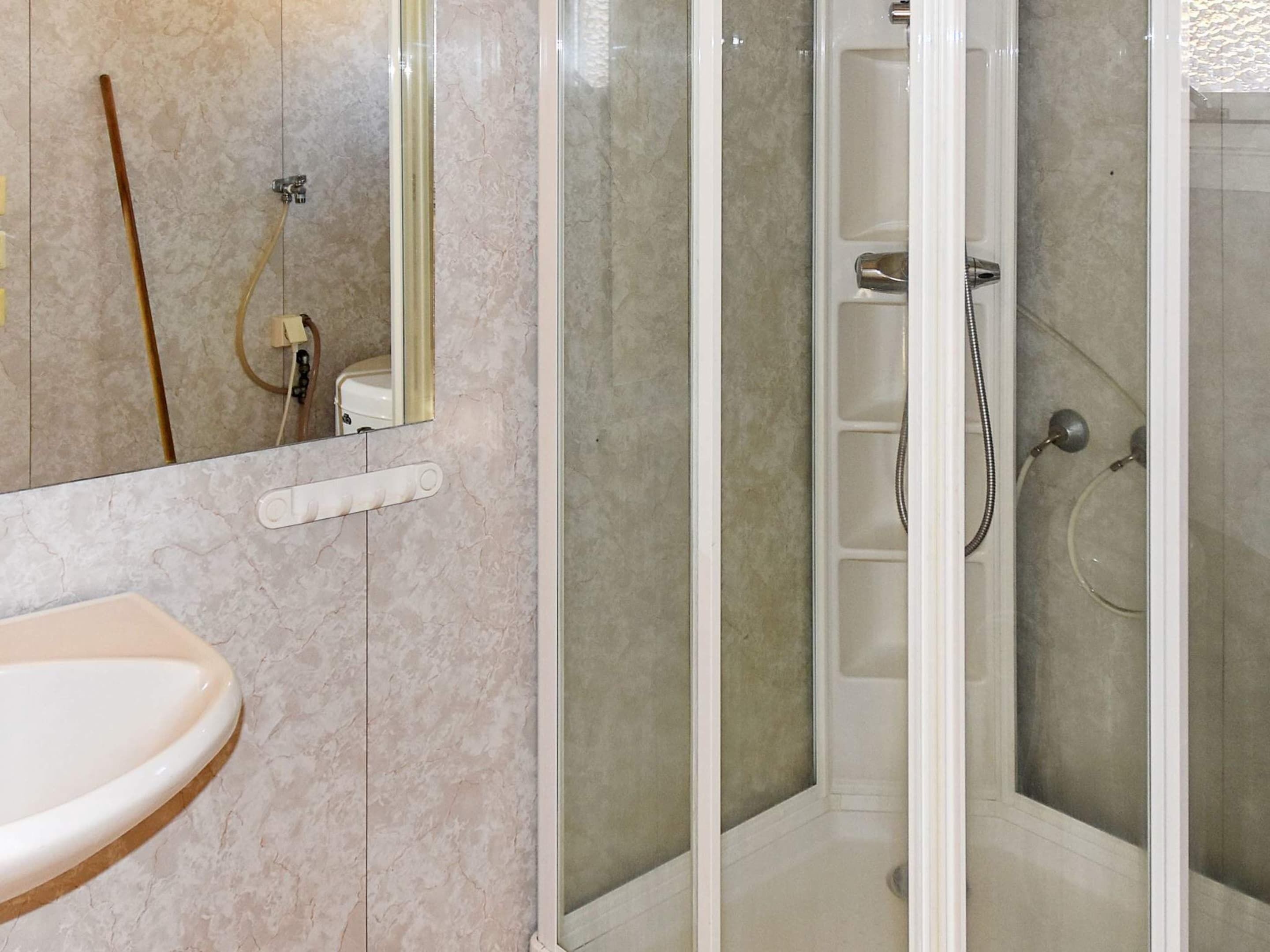 Ein Badezimmer mit einem weißen Waschbecken, einer Duschkabine aus Glas und einer Wand mit Marmorfliesen.