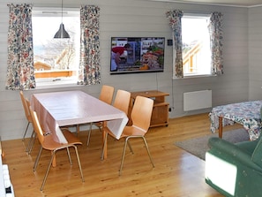 Quarto com mesa de jantar, cadeiras, televisão e vista para o exterior.
