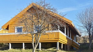 A wooden house with a balcony, a tree in front, and a clear sky.