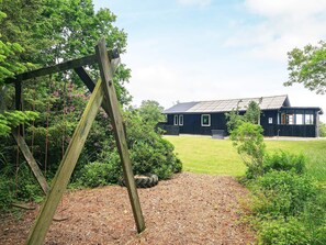 A wooden swing set in a garden leading to a black house with a metal roof. - 5 Person Holiday Home in Roslev-by Traum (Roslev)