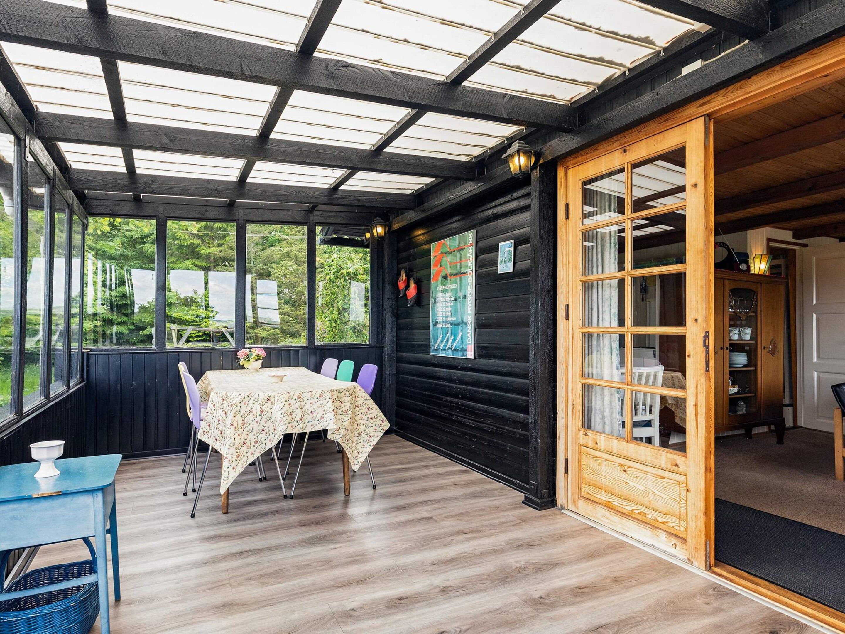 A covered outdoor seating area with a table and chairs, a wooden cabinet, and a view of greenery outside.
