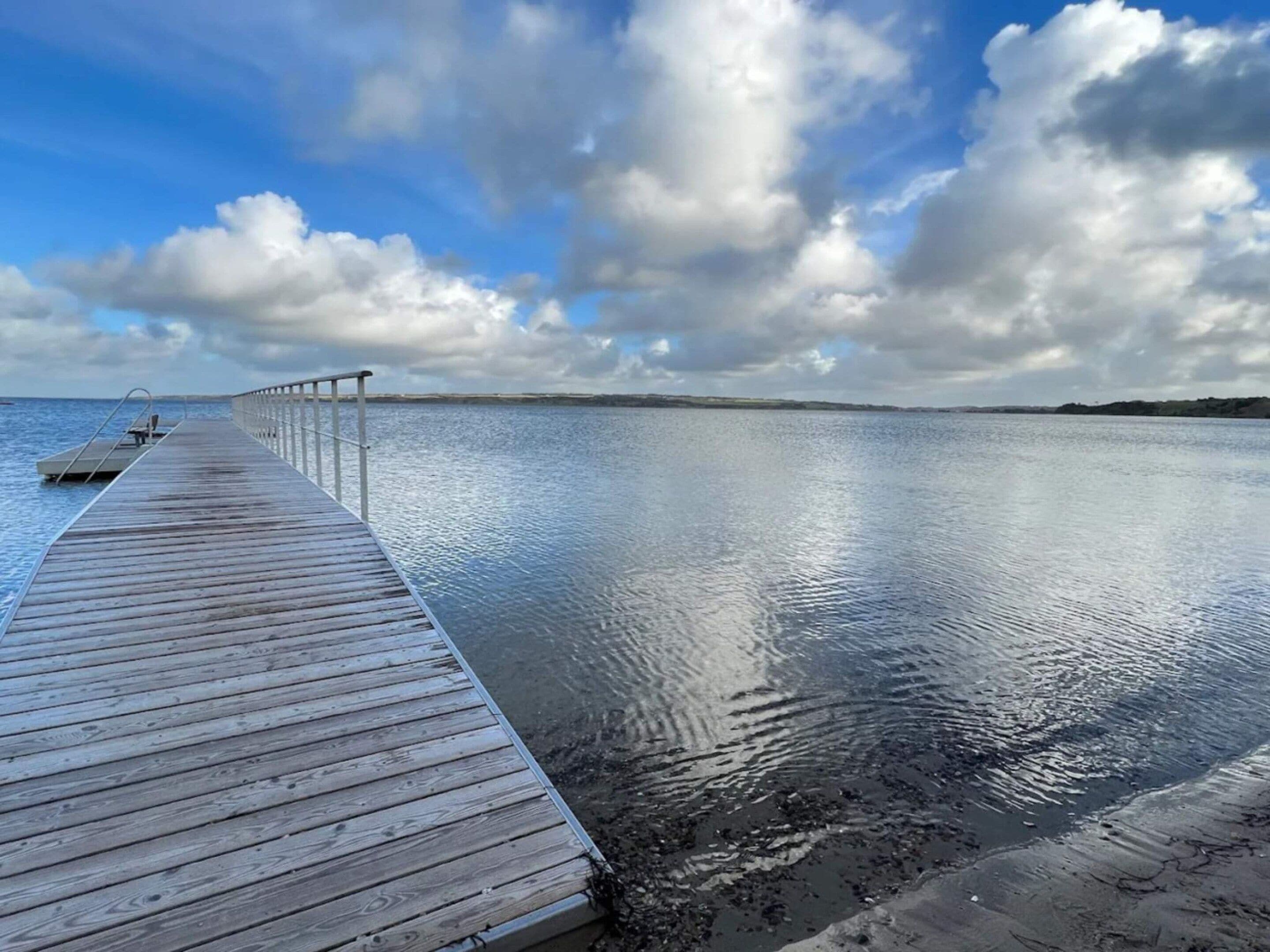 A wooden pier extending into calm water with a clear sky above.
