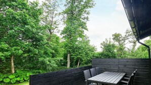 An outdoor patio with a wooden table and chairs, surrounded by a black fence and lush greenery.