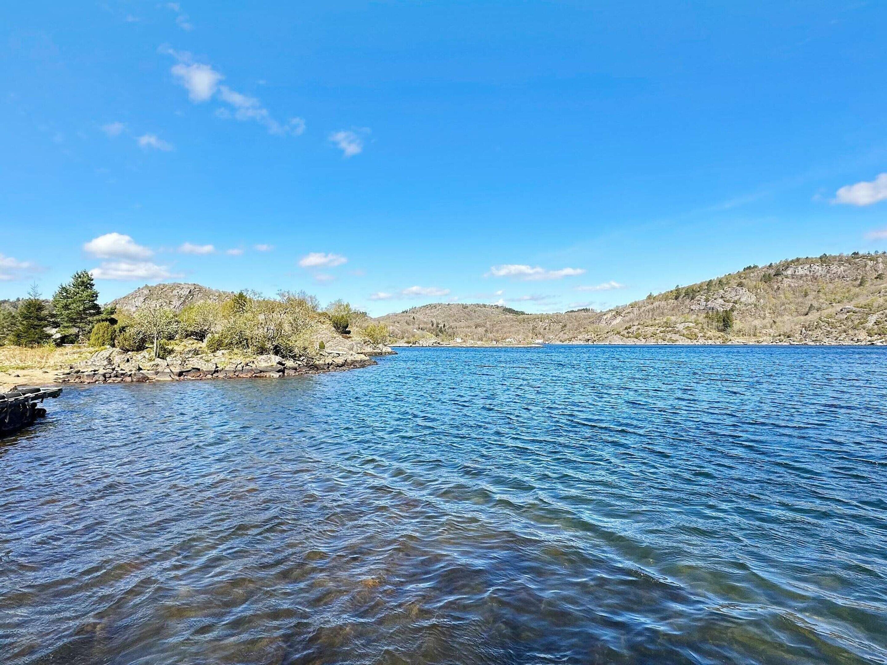 A calm lake with clear blue water, surrounded by rocky hills and sparse vegetation.