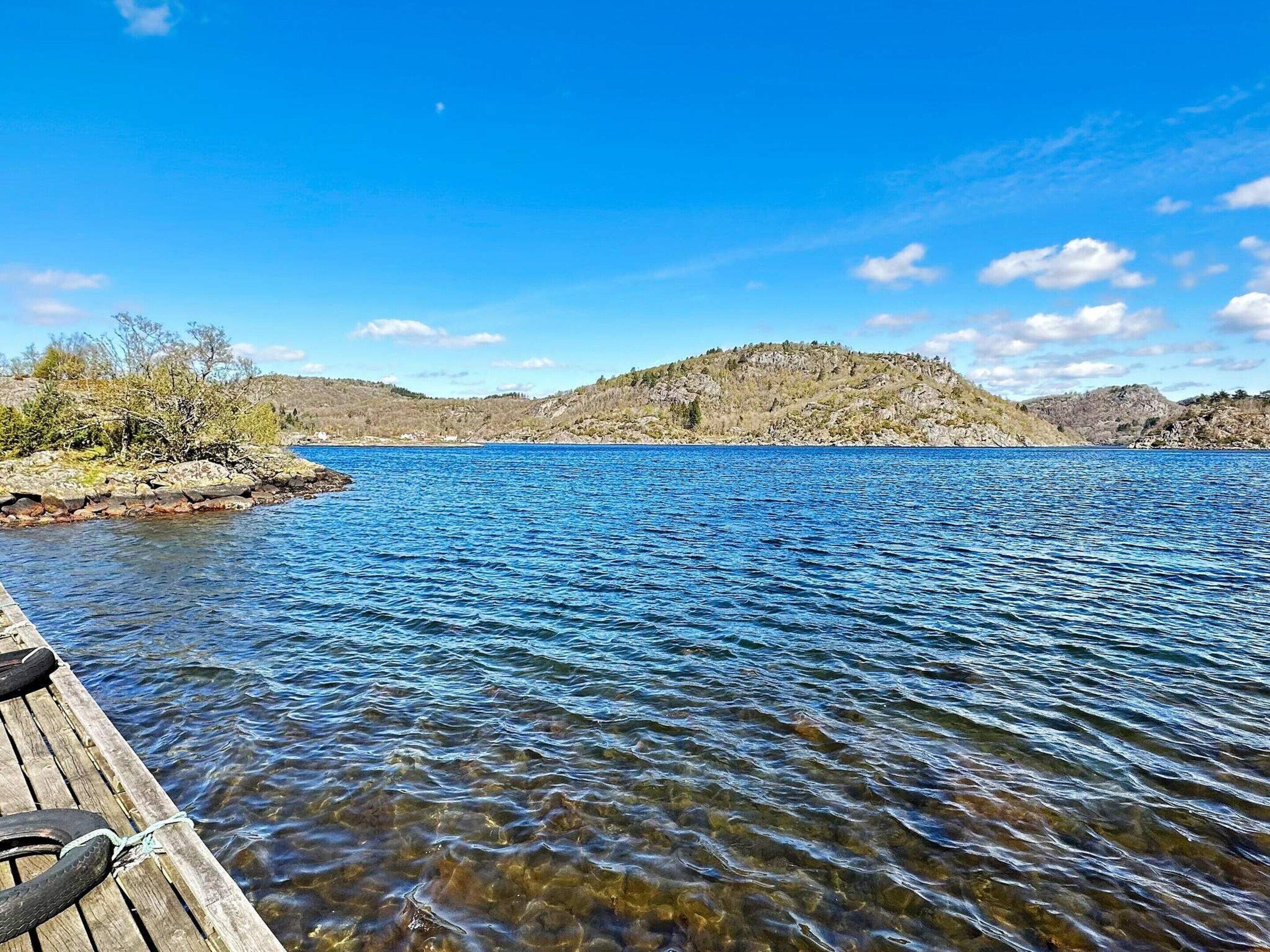 A wooden dock extending into a calm lake with clear water, surrounded by rocky hills and sparse vegetation.