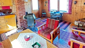 A cozy cabin interior with wooden walls, a brick fireplace, a dining area with a table and chairs, and a living room with a sofa and a patterned rug. - 5 Person Holiday Home in Farsund (Farsund)