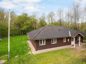 A wooden cabin with a tiled roof, surrounded by a grassy area and trees.