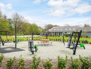An outdoor gym area with exercise equipment, a picnic table, and a building in the background.