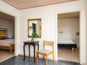 A bedroom with a bed, a chair, a table with a plant, and a mirror on the wall.