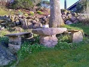 Um cenário natural ao ar livre com um banco de pedra, uma árvore e um monte de pedras.