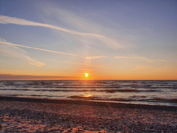 A sunset over a rocky beach with waves. - 10 Person Holiday Home in Ebeltoft-by Traum (Ebeltoft)