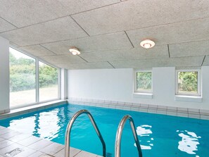 An indoor swimming pool with clear water, two windows, and a tiled ceiling.