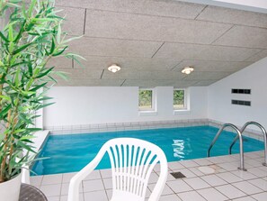 An indoor swimming pool with clear blue water, a white chair, and a potted plant.