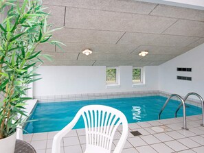 Una piscina interior con agua cristalina, una silla blanca y una planta en maceta.