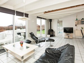 Una sala de estar moderna con un sofá, una mesa de comedor y un televisor. Cuenta con una chimenea y un balcón con sillas.
