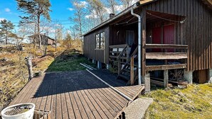 Ein rustikales Holzhäuschen mit Veranda, umgeben von Bäumen und blauem Himmel.