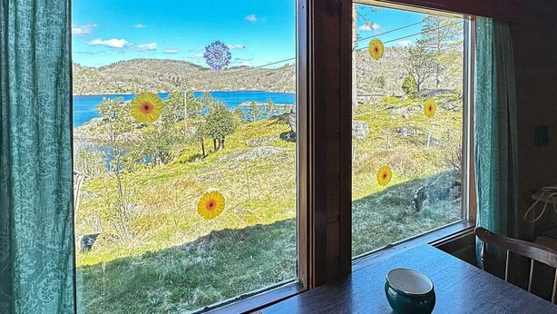 Ein Zimmer mit großem Fenster und Blick auf eine Küstenlandschaft mit Hügeln und einer Brücke.