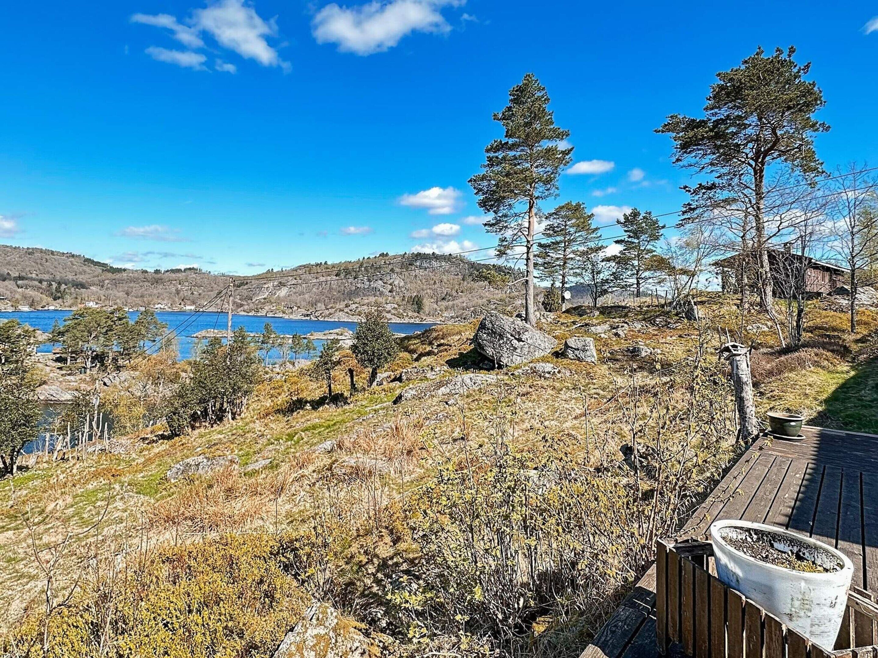 A wooden deck overlooking a lake with trees and a distant cabin.