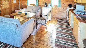 Ein gemütliches Blockhaus-Interieur mit Holzboden, einer Couch, einem Esstisch, einer Küchenzeile mit Herd und Kühlschrank.