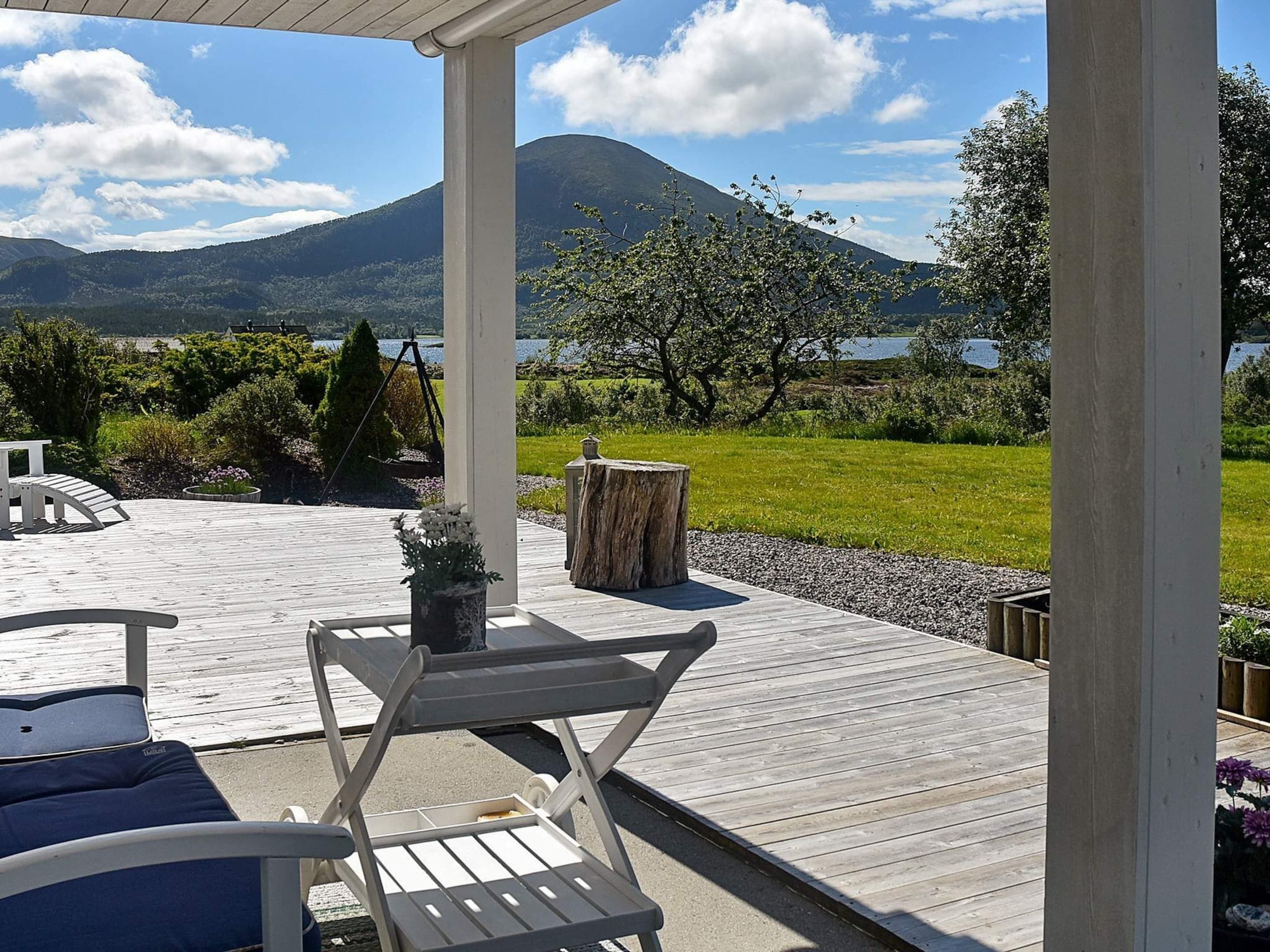 A wooden deck with outdoor furniture, a view of a lake, and a mountain in the background.