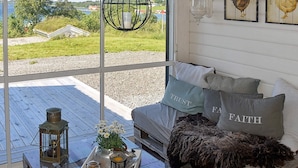 A cozy room with a large window, a wooden deck, a glass table with a tray of items, and a sofa with decorative pillows. - Holiday Home in Tornes I Romsdal (Hustadvika)