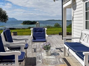 A wooden deck with outdoor seating, a view of a lake, and a distant island.
