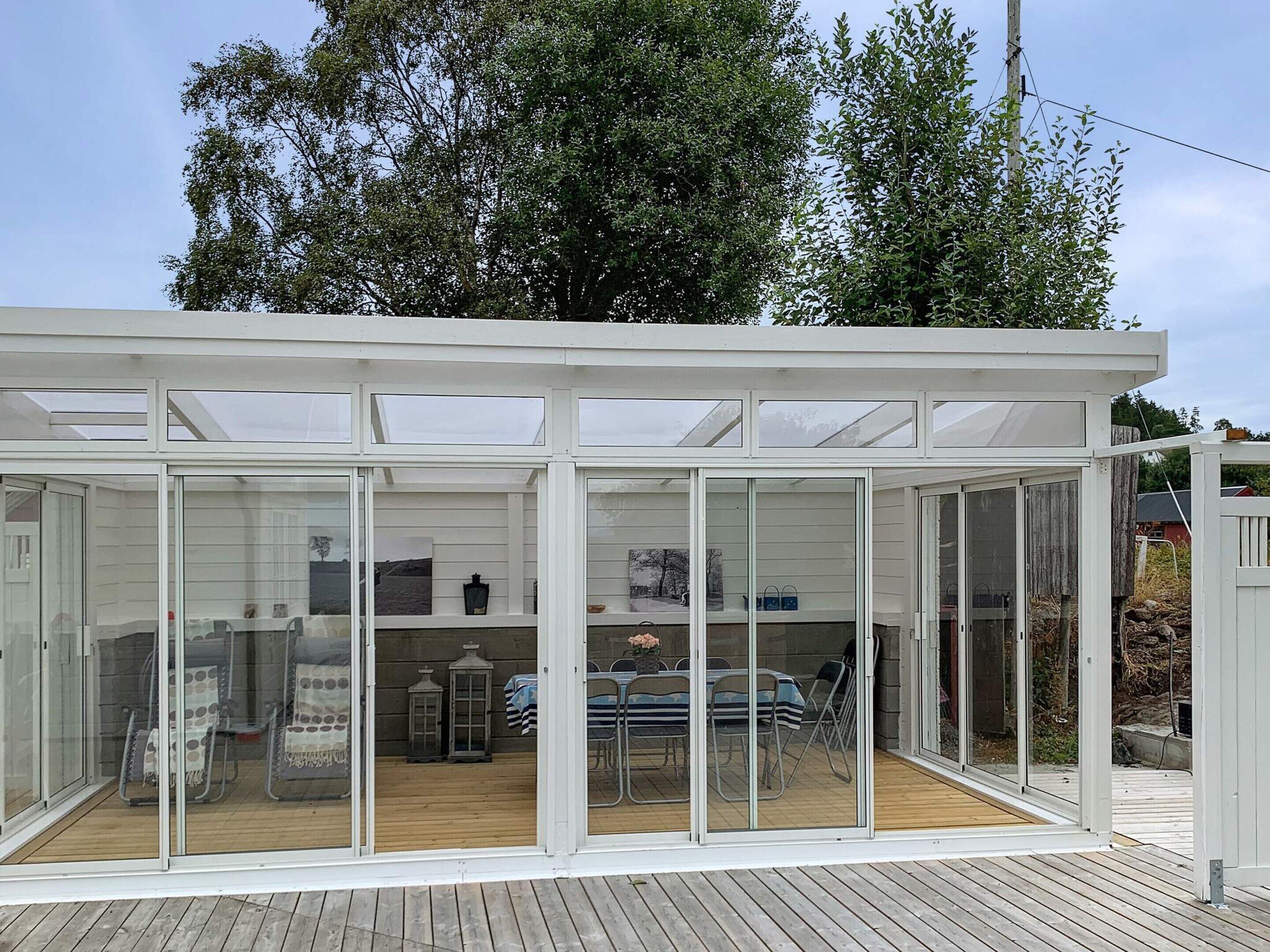 Eine verglaste Terrasse mit Holzdeck, Gartenmöbeln und Blick auf die Umgebung.