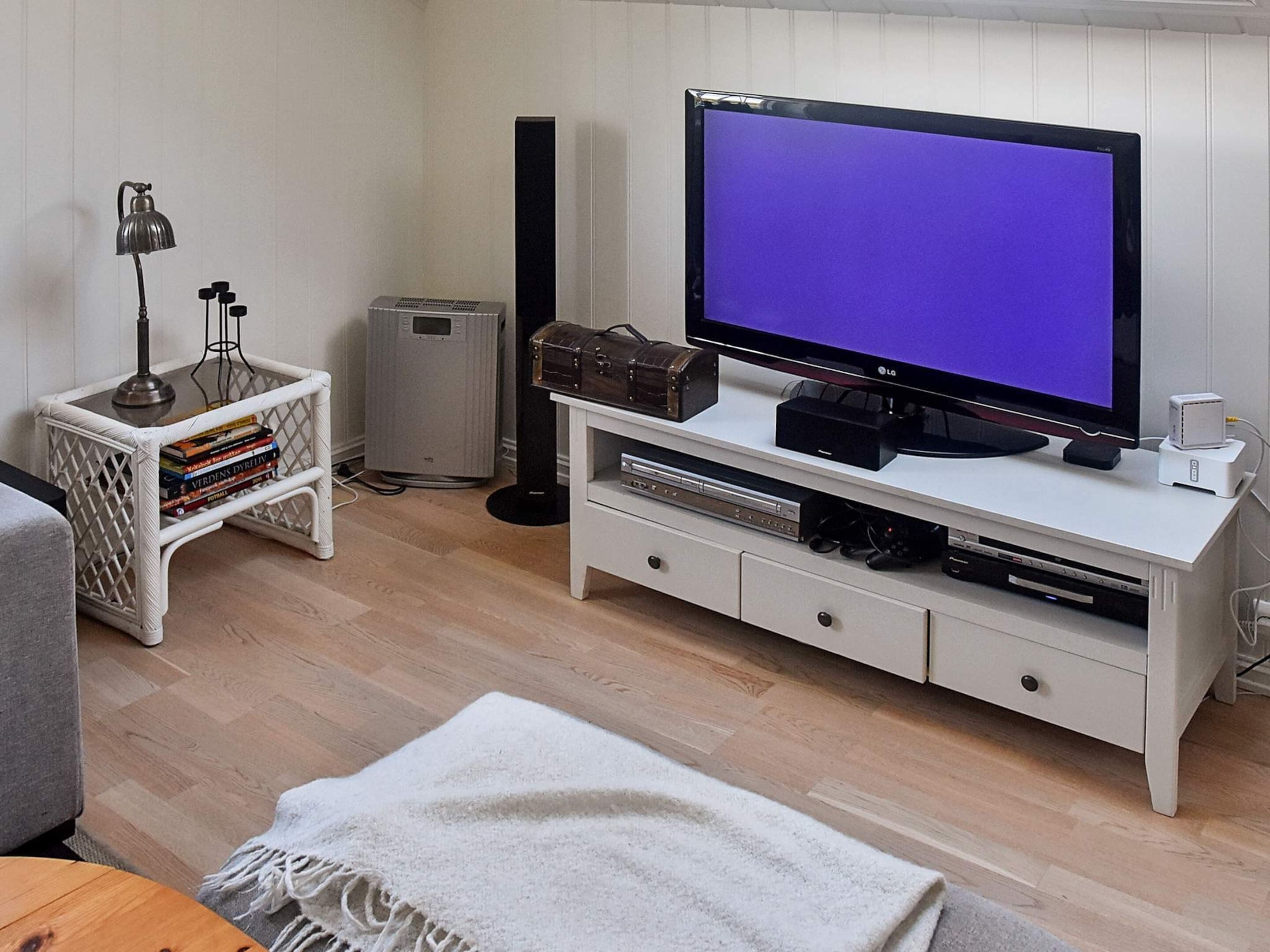 A living room with a flat-screen TV, a small side table with books, a lamp, and a speaker.