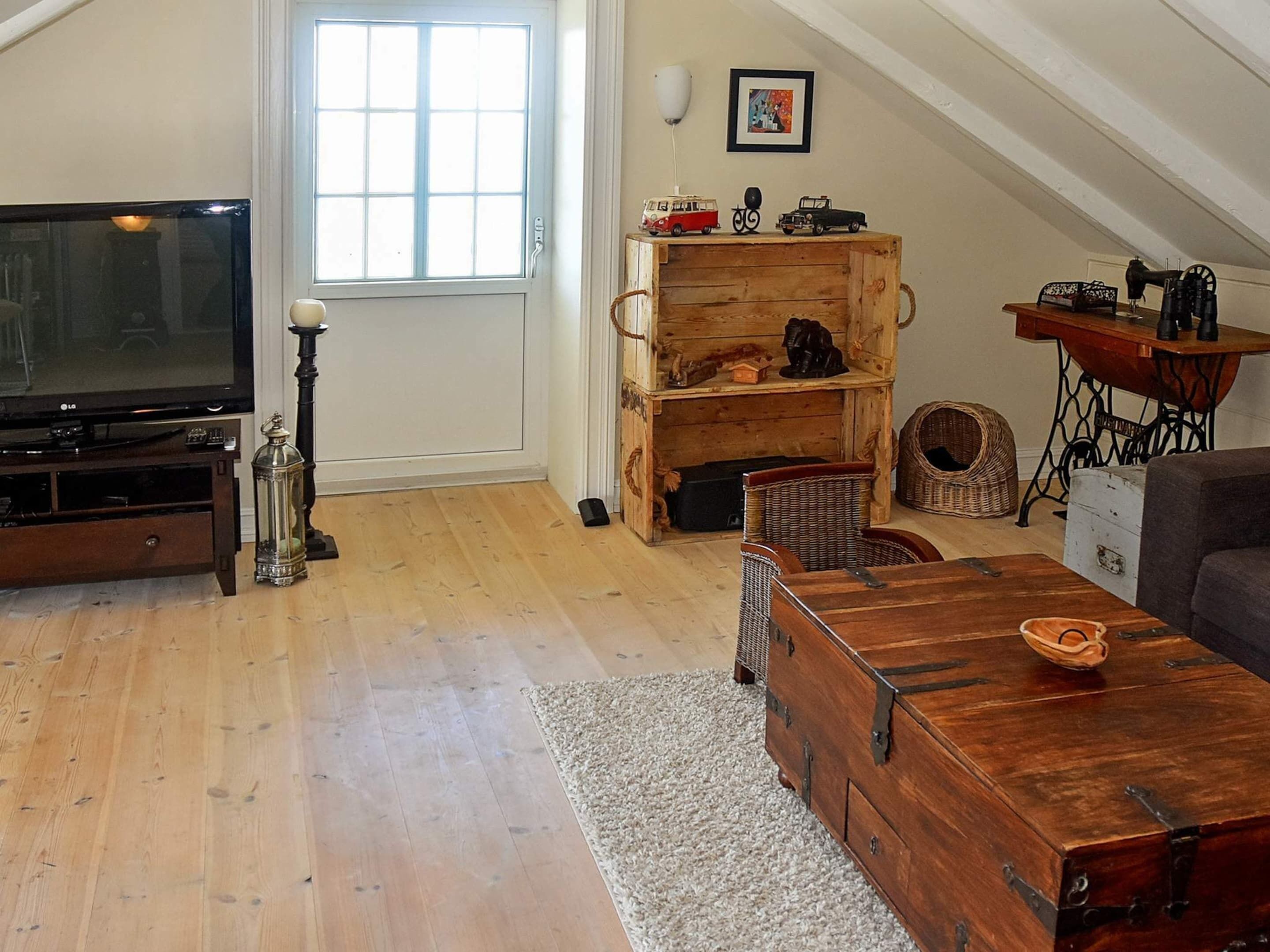 A living room with a television, wooden furniture, a window, and a ceiling with exposed beams.