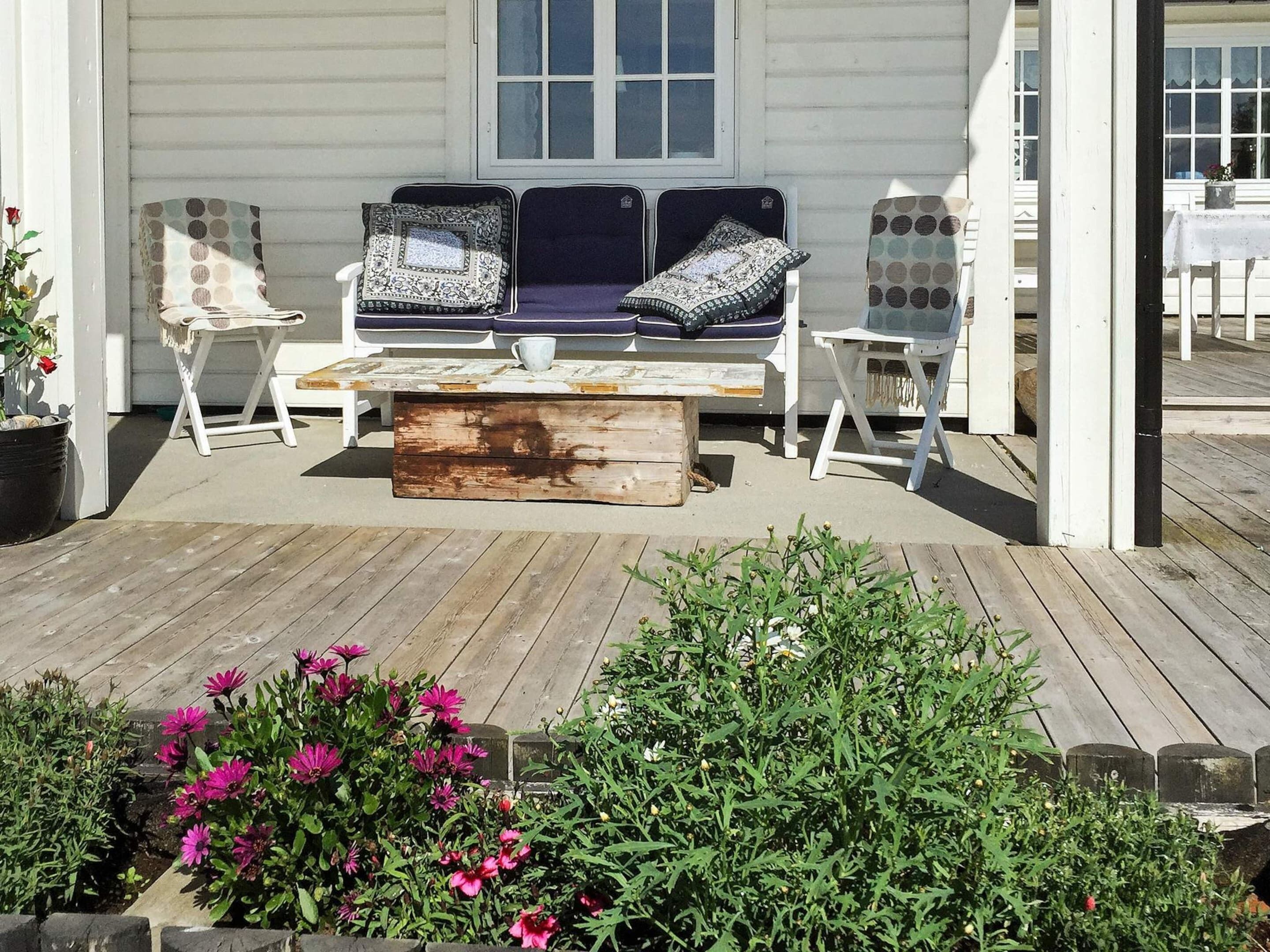 An outdoor seating area with a wooden coffee table, two cushioned chairs with patterned cushions, and a bench.