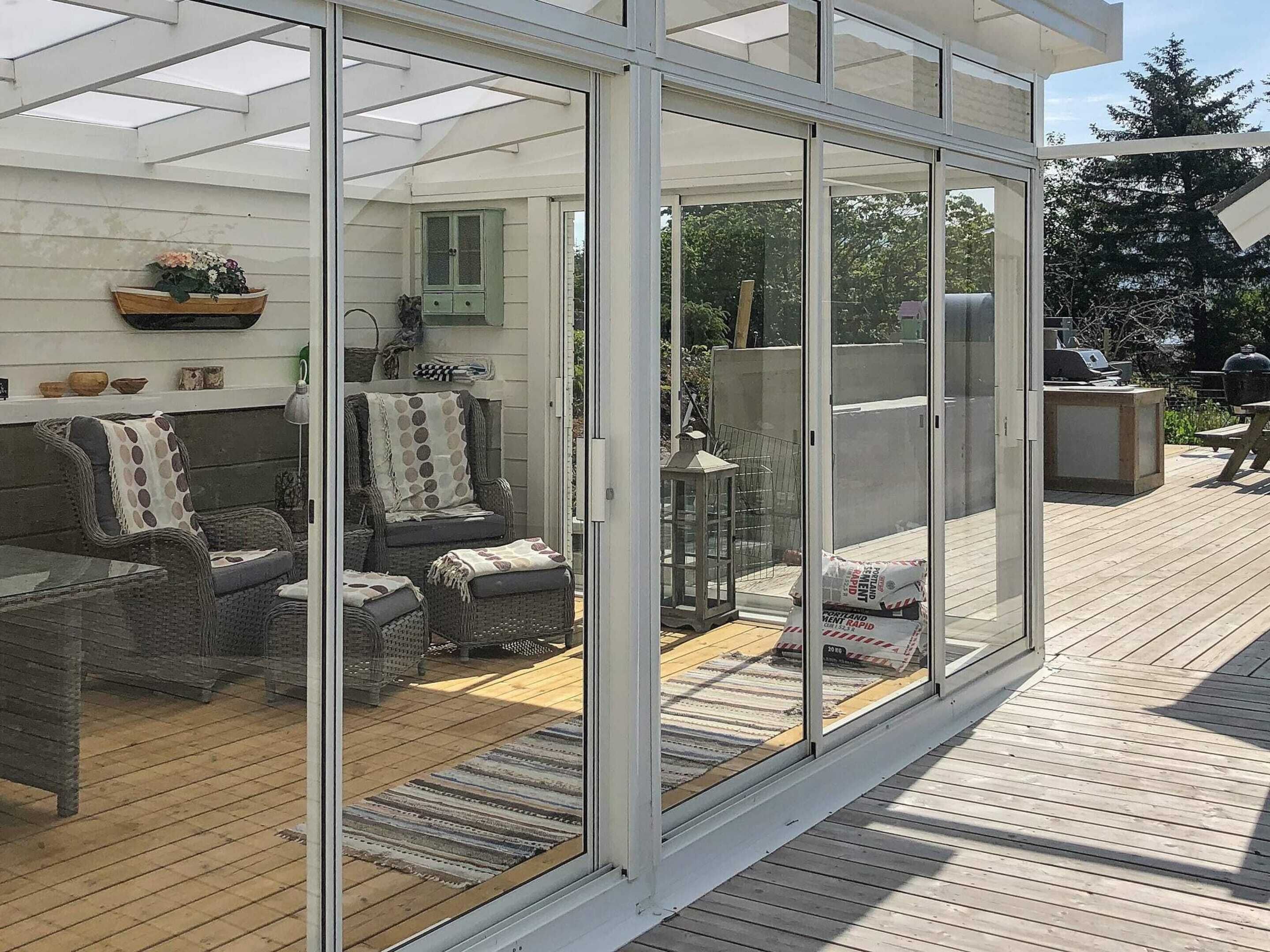 Eine überdachte Terrasse mit Korbmöbeln, einer Laterne und Grillplatz.