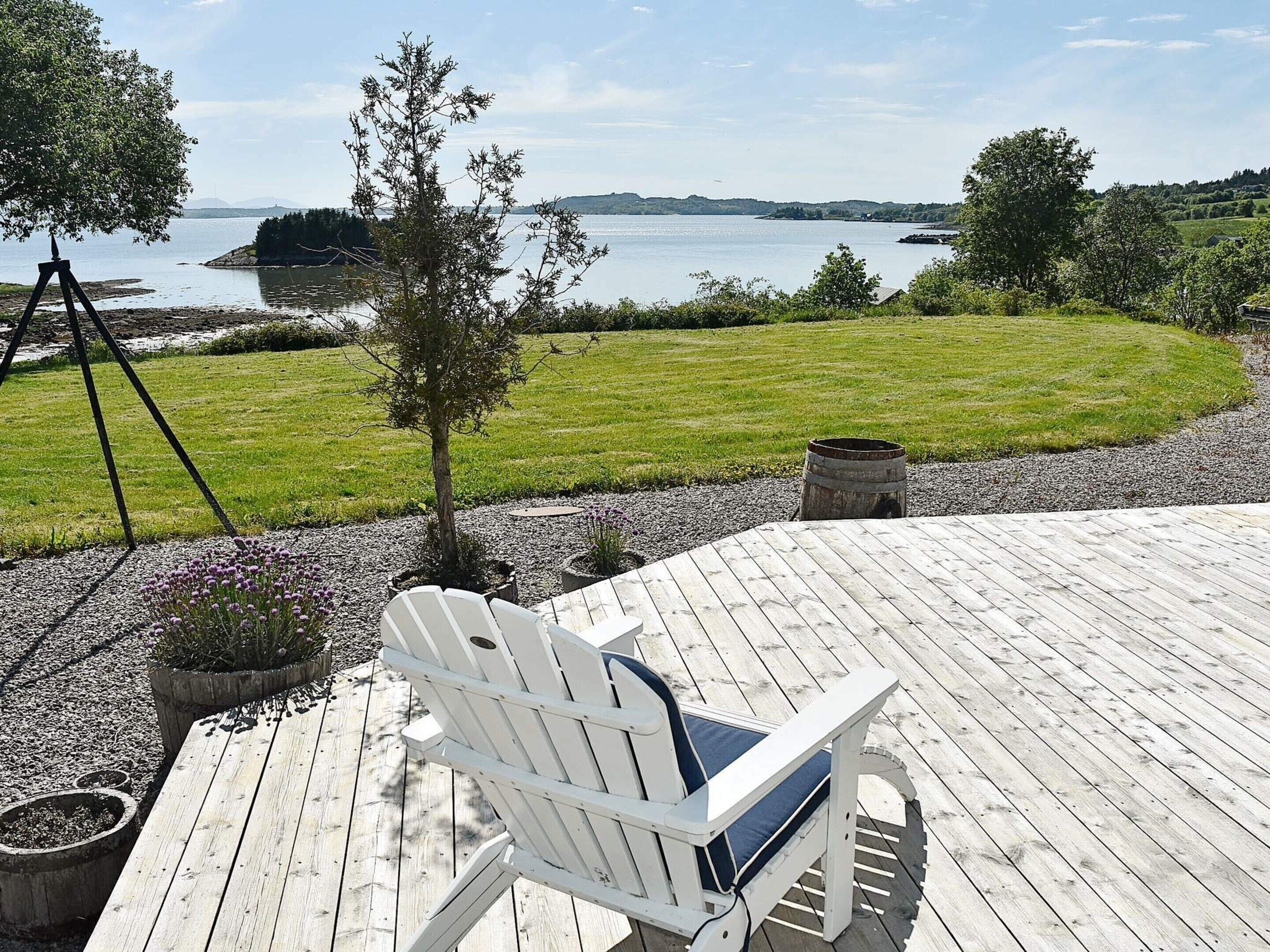 Puinen terassi, jossa on valkoinen Adirondack-tyylinen tuoli, keinuteline ja näkymä järvelle ja kaukaisiin kukkuloille.