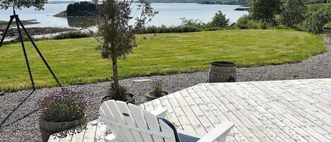 Puinen terassi, jossa on valkoinen Adirondack-tyylinen tuoli, keinuteline ja näkymä järvelle ja kaukaisiin kukkuloille.