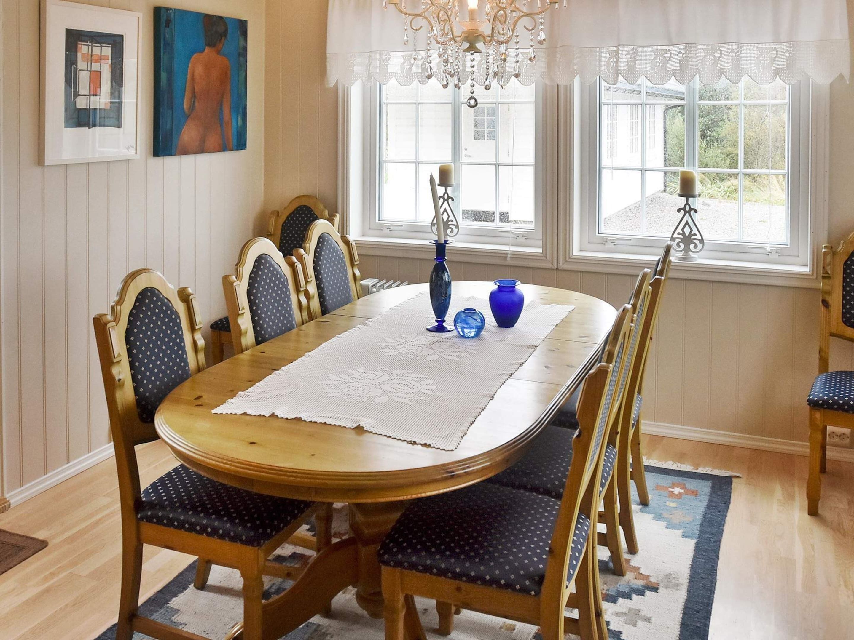 A dining room with a wooden table, six chairs, a lace table runner, and a chandelier.