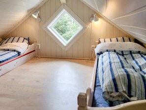 Une petite chambre mansardée avec deux lits, une lucarne et des poutres en bois.