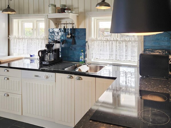 Une cuisine avec des meubles blancs, un plan de travail noir, une machine à café et un grille-pain.