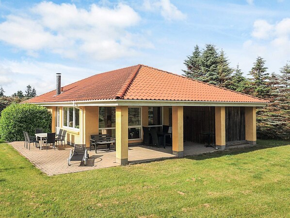 A single-story house with a tiled roof, a covered patio area with outdoor furniture, and a well-maintained lawn.