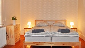 A double bed with a wooden frame, two bedside tables with lamps, a small wooden dresser, and a plant on the dresser. - Holiday Home in Vargön (Västra Tunhem)