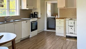 A kitchen with white cabinets, a stove, a sink, and a coffee maker. - Holiday Home in Vargön (Västra Tunhem)