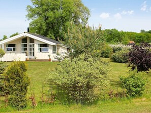 A single-story house with a large front porch, surrounded by a well-maintained lawn and various shrubs.