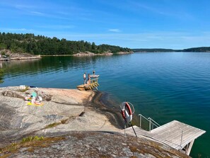 A dock extending into a calm lake with a rocky shoreline and a forested hill in the background. - 6 Person Holiday Home in Brastad (Brastad)